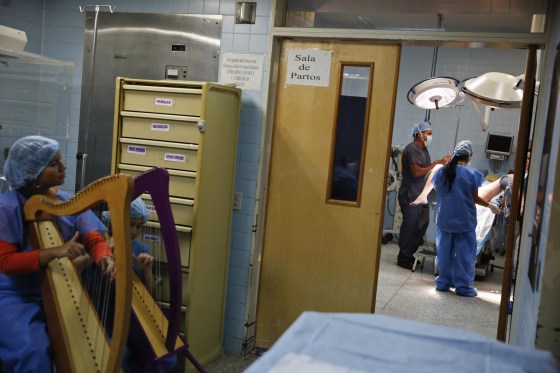 Image: Members of \"El Sistema\" play harps, as part of their \"New Members\" program, outside of the operating room where a woman is giving birth to her son at a public maternity hospital in Caracas