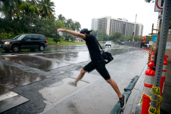 Image: A man jumps over a puddle as he prepares to board a bus in Honolulu on Sunday.