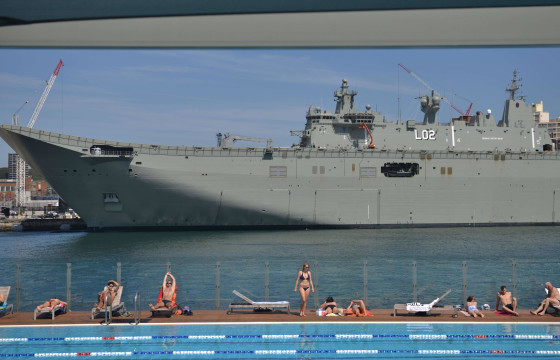Sunbathers relax beside a swimming pool in Sydney in front of HMAS Canberra, which is berthed at the city's Garden Island naval base.
