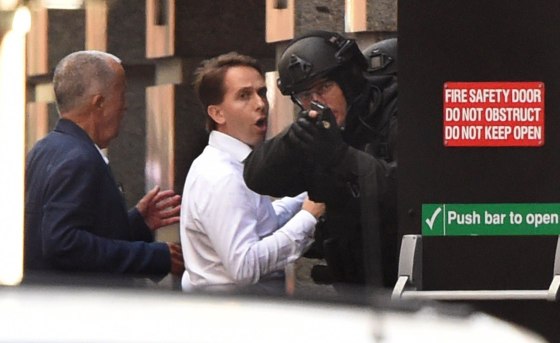 Two hostages run for cover behind a policeman during a hostage siege in the central business district of Sydney on December 15, 2014. Three people ran out of a Sydney cafe where a gunman has taken hostages and displayed an Islamic flag against the window, police said December 15, adding that no one has yet been harmed.