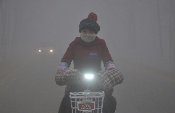 Image: A woman rides her electric bicycle along a street amid thick haze in Chiping county