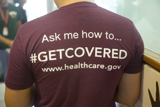 Image: A volunteer healthcare worker wears a T-shirt encouraging people to sign up for the new healthcare program.