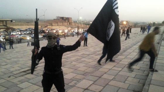 Image: A fighter of the ISIS holds a flag and a weapon on a street in Mosul