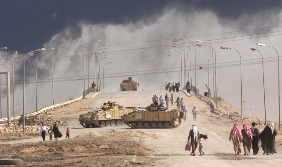 Image: Civilians on foot pass tanks on a bridge near the entrance to the besieged city of Basra March 29, 2003 in Iraq.