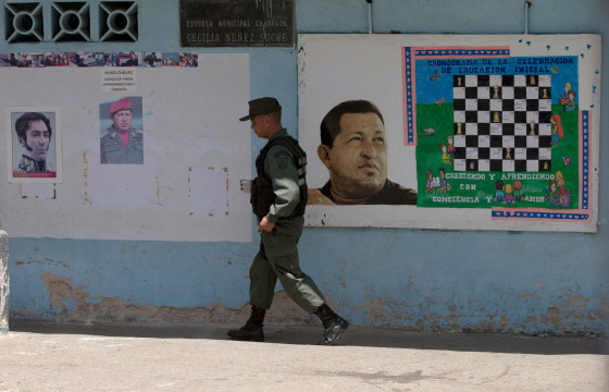 A Bolivarian National Guard officer walks near images of the late Venezuelan President Hugo Chavez and Independence hero Simon Bolivar, left, at a poll station in Caracas, Venezuela, Sunday, May 17, 2015.