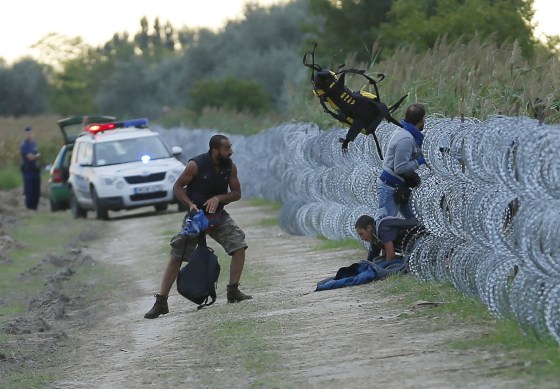 Image: Hungarian police positioned nearby watch as Syrian migrants climb under a fence to enter Hungary at the Hungarian-Serbian border near Roszke