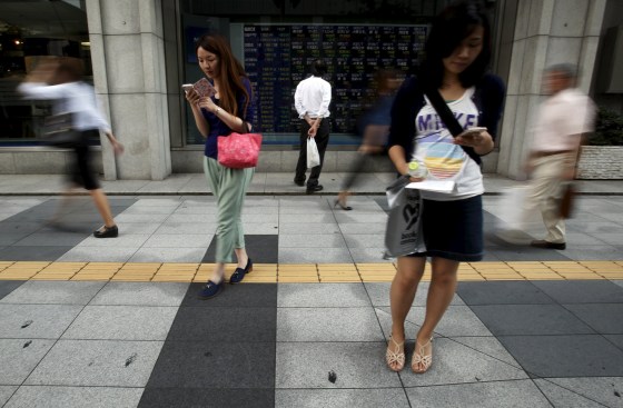 Image: A pedestrian looks at an electronic board showing the various stock prices outside a brokerage in Tokyo