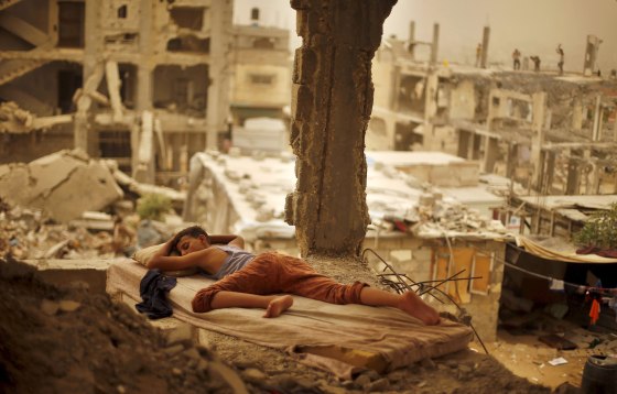 Image: Palestinian boy sleeps on a mattress inside the remains of his family's house that witnesses said was destroyed by Israeli shelling during a 50-day war in 2014 summer during a sandstorm in Gaza