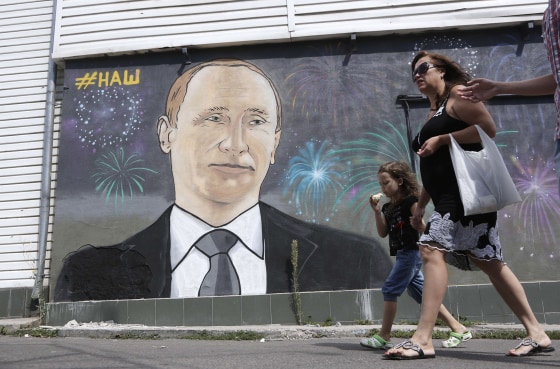Image: People walk past a mural depicting Russia's President Vladimir Putin
