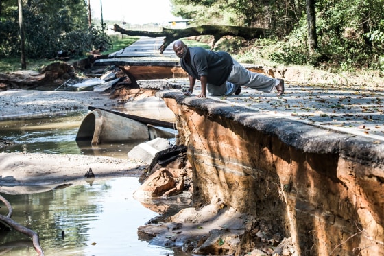 Image: A man observes severe road damage after floodwaters recede