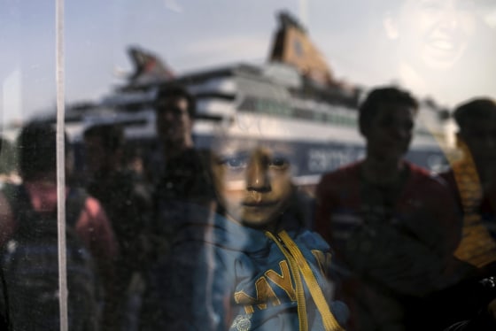 Image: A migrant boy is seen through a bus window as refugees and migrants arrive aboard the passenger ferry Blue Star Patmos from the island of Lesbos at the port of Piraeus
