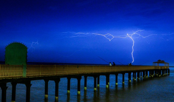 Lightning flashes over people fishing on the coast near Kuwait City, Kuwait.