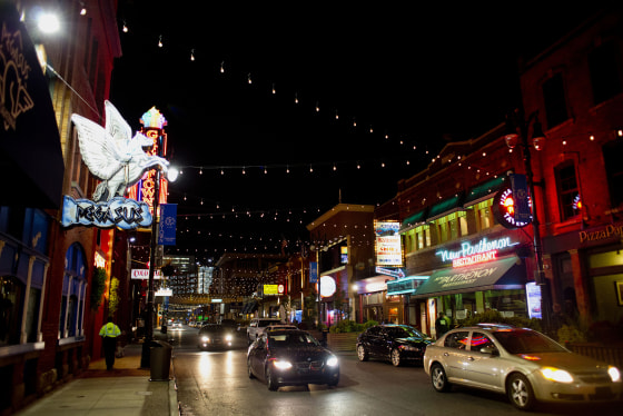 Lights are strung across the street at night as cars move along Monroe Avenue in the Greektown neighborhood of downtown Detroit, Michigan, U.S., on Tuesday, Oct. 13, 2015. Ten months after emerging from a record $18 billion municipal bankruptcy, Detroit is functioning in ways unseen for months and even years -- street lights are on, parks get mowed, municipal debt is sold on the public market and the police are training civilians to manage traffic at clogged intersections.