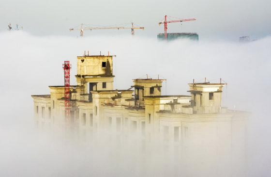 Image: Cranes and residential buildings under construction are seen among thick fog in Anyang
