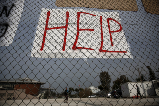 A placard is hung on a fence as migrants make their way inside the premises of a former Olympic indoor stadium in Faliro, southern Athens, on Tuesday, Dec. 15, 2015.