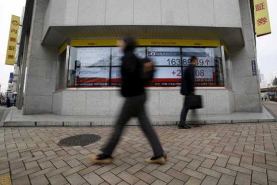 Pedestrians walk pass an electronic board outside a brokerage in Tokyo