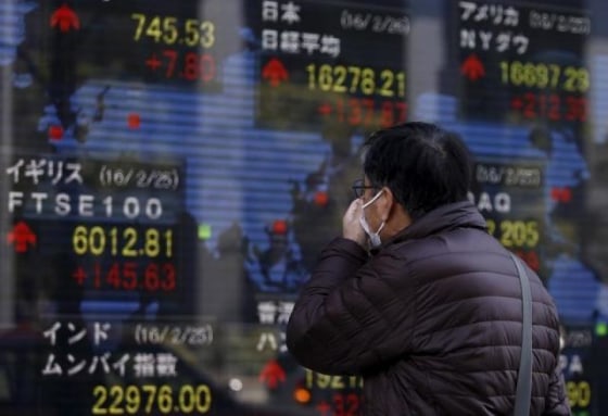 A pedestrian looks at an electronic board showing the stock market indices of various countries outside a brokerage in Tokyo