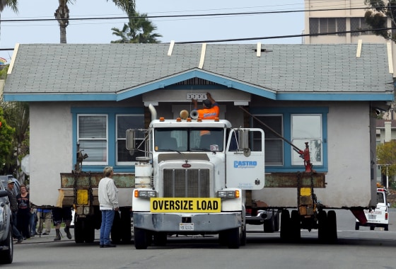Image: Home owner Anne Wilson asks for the house numbers as workers remove her old home for recycling and resale from its neighborhood in San Diego