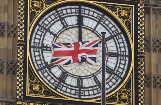 A British Union flag flutters in front of one of the clock faces of the 'Big Ben' clocktower of The Houses of Parliament in central London