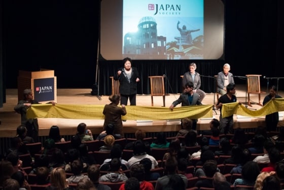 Thurlow speaking at a Japan Society event. The yellow banner contains 331 names of girls from Thurlow's school who died on Aug. 6, 1945.