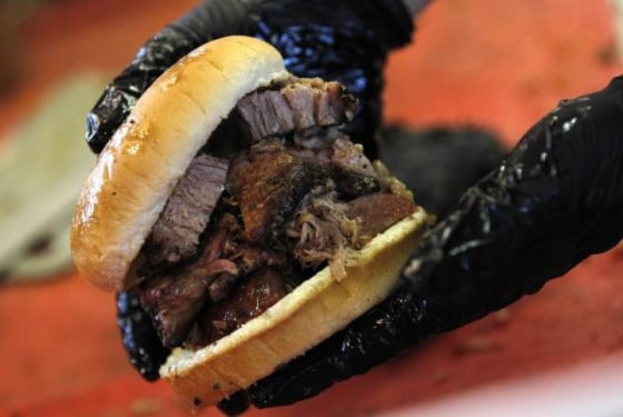 Johnson holds \"The Trio\", a three meat sandwich featuring jalapeno sausage, pulled pork and sliced brisket, at Stillwater Barbeque in Abilene