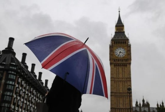 A woman holds a Union flag umbrella in front of the Big Ben clock tower and the Houses of Parliament in London