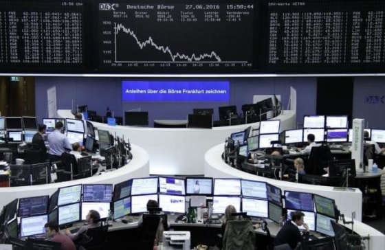 Traders work at their desks in front of the German share price index, DAX board, at the stock exchange in Frankfurt