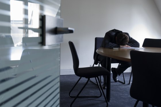Businessman resting head on table in meeting room, view through door