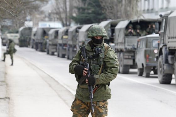 Image: Armed servicemen wait in Russian army vehicles outside a Ukranian border guard post in the Crimean town of Balaclava