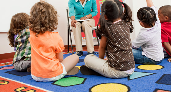 Teacher and children sitting on floors with hands raised