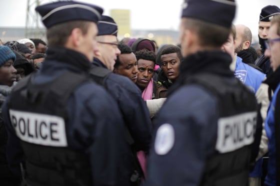 Image: Police officers standby as migrants line-up to register at a processing centre in Calais