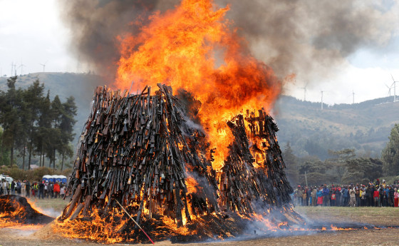 Image: Civilians watch as an assortment of 5250 illicit firearms and small weapons, recovered during various security operations