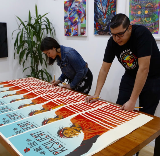 Artists Ernesto Yerena and Ayse Gursoz signing one of the posters in the "We the People" art series.
