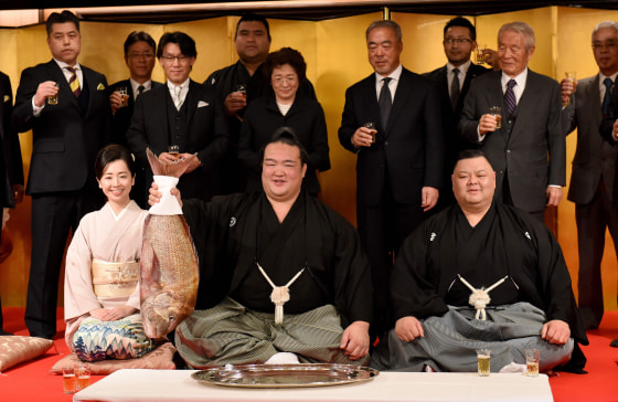Image: Accompanied by stable master Tagonoura (bottom-R), Tagonoura's wife (bottom-L) and supporters, sumo wrestler Kisenosato (C) holds up a big sea bream to celebrate his promotion to the top rank of "yokozuna."