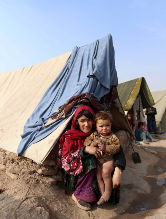 Image: People driven from their homes by violence sit in front of a tent