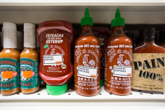 A "Made By Refugee" sticker on a bottle of Sriracha hot sauce.