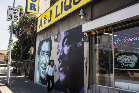 Image: A woman walks past a mural of Cesar Chavez, left, and Martin Luther King Jr., in South Central Los Angeles