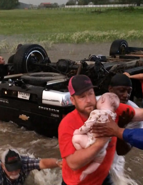 Image: A man rescues an infant that was trapped after a vehicle flipped over on a flooded highway in Canton