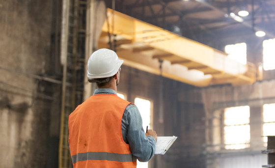 Steel worker with clipboard looking up in factory