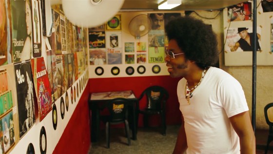 Alex Cuba in Cuban studio looking at albums on the wall