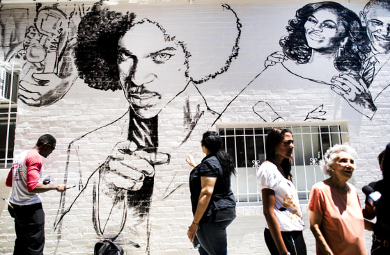 Image: Muralist Aniekan Udofia, left, works on his new mural