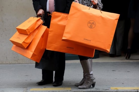 A couple walk with Hermes shopping bags as they leave a Hermes store in Paris