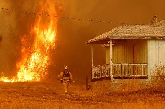 Image: A firefighter walks near a home as flames from the fast-moving Detwiler fire approach on July 19.