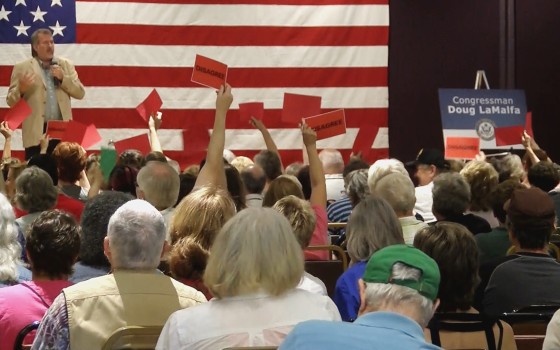 Audience members hold up red cards that say "Disagree" at a town hall in Chico, California, held by Rep. Doug LaMalfa.