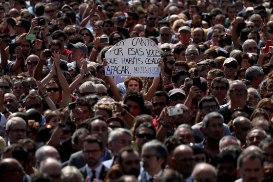 Image: A woman holds a sign that reads \"I sing today for those voices that you have dared to shut up. We are not afraid\" while observing a minute of silence at Placa de Catalunya, a day after a van crashed into pedestrians at Las Ramblas in Barcelona