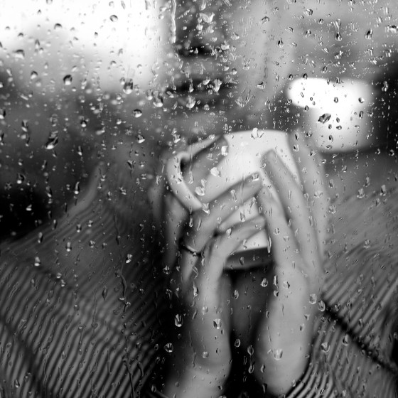 Image: A woman watches the rain from behind a window