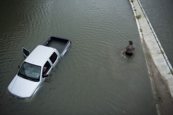 Image: A truck driver walks past an abandoned truck while checking the depth of an underpass