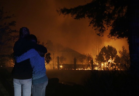 Image: Two people hug as they watch houses burn in Santa Rosa