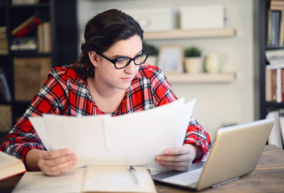 Image: A woman looks over papers over a laptop