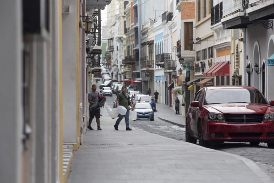 Two men carry equipment and bottles to fill up with water down a usually busy street in the Old San Juan neighborhood on Wednesday, Oct. 18, 2017 in San Juan, Puerto Rico.